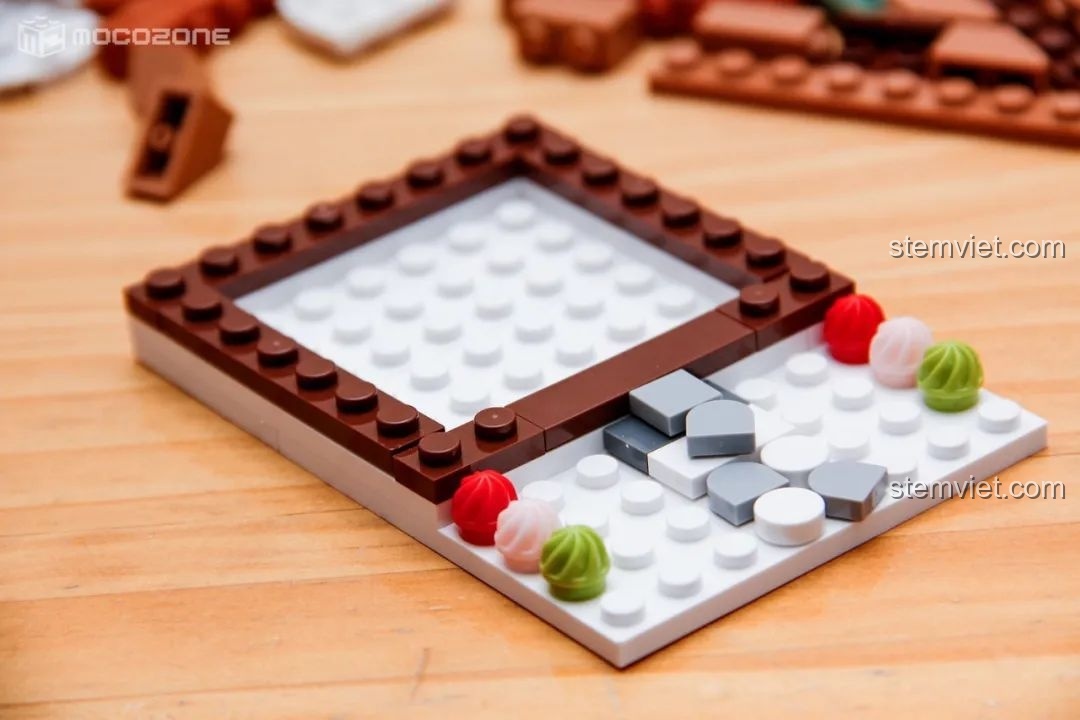 Phần đế của ngôi nhà bánh gừng đang được lắp ráp, với nền trắng mô phỏng tuyết và các chi tiết trang trí nhỏ.