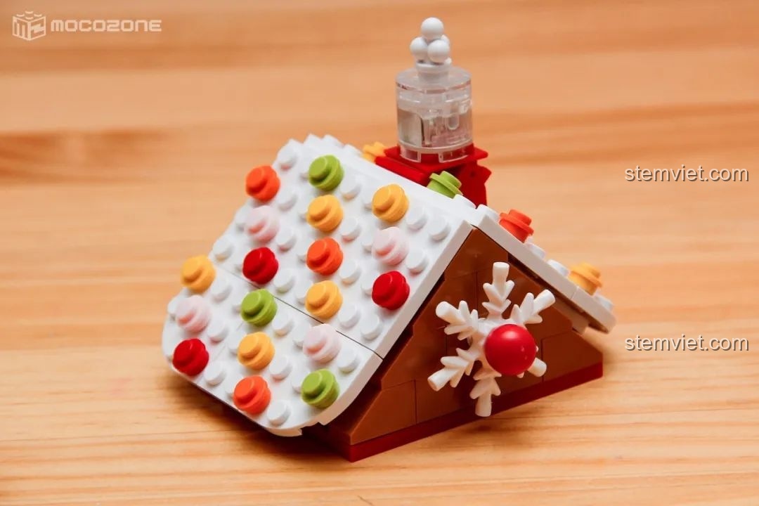 Mô hình ngôi nhà bánh gừng đã hoàn thành, với mái nhà đầy kẹo và cây thông Noel nhỏ bên cạnh.