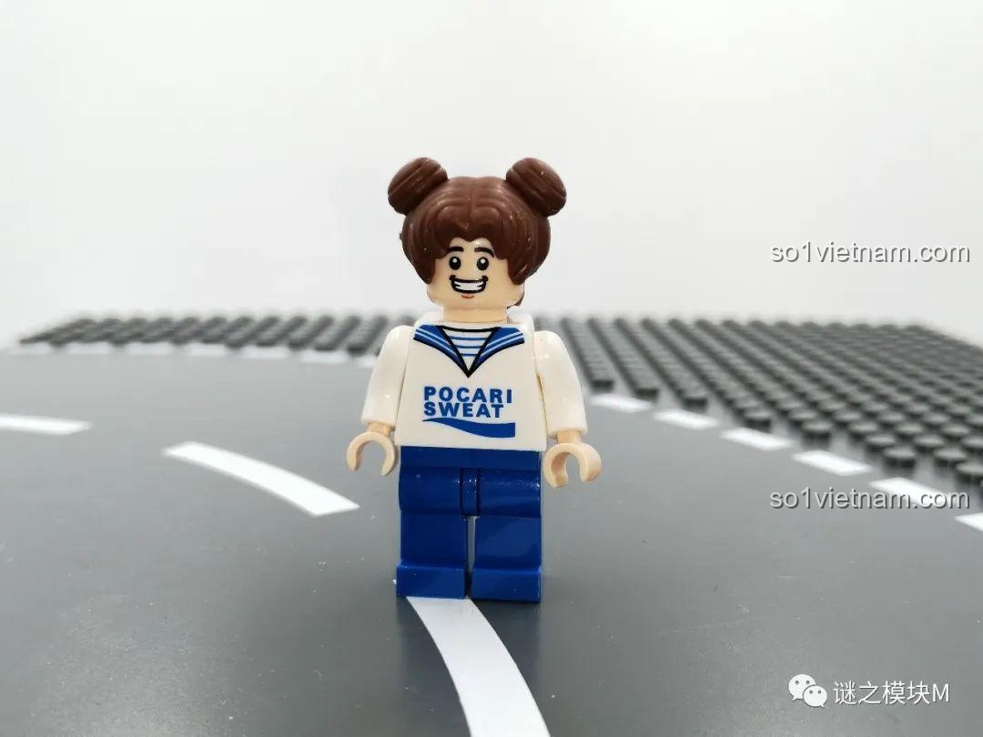 Minifigure Pocari Sweat với kiểu tóc búi đáng yêu, mặc áo Pocari Sweat và quần xanh, đứng trên nền gạch lắp ráp.