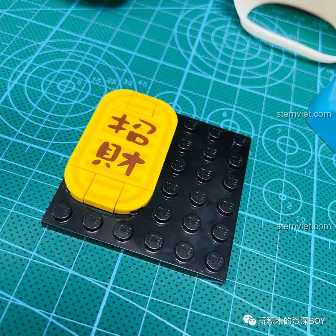 Mô hình Doraemon Mèo Thần Tài K20412 đã hoàn thiện, ngồi trên thảm cắt, cầm bảng 'Chiêu Tài' với biểu cảm đáng yêu.