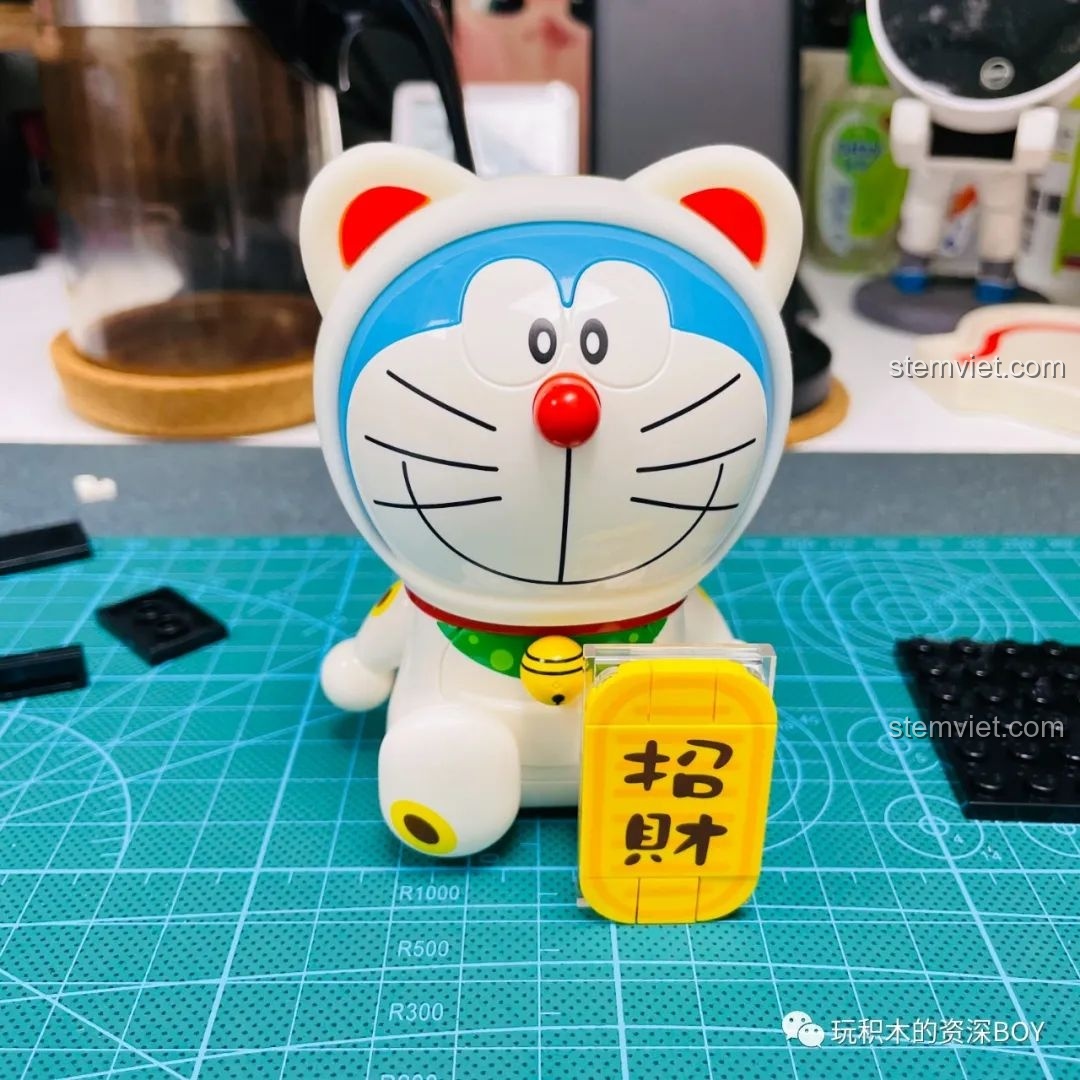 Mô hình Doraemon Mèo Thần Tài K20412 đã hoàn thiện đặt cạnh hộp sản phẩm, cho thấy sự giống nhau đáng kinh ngạc.