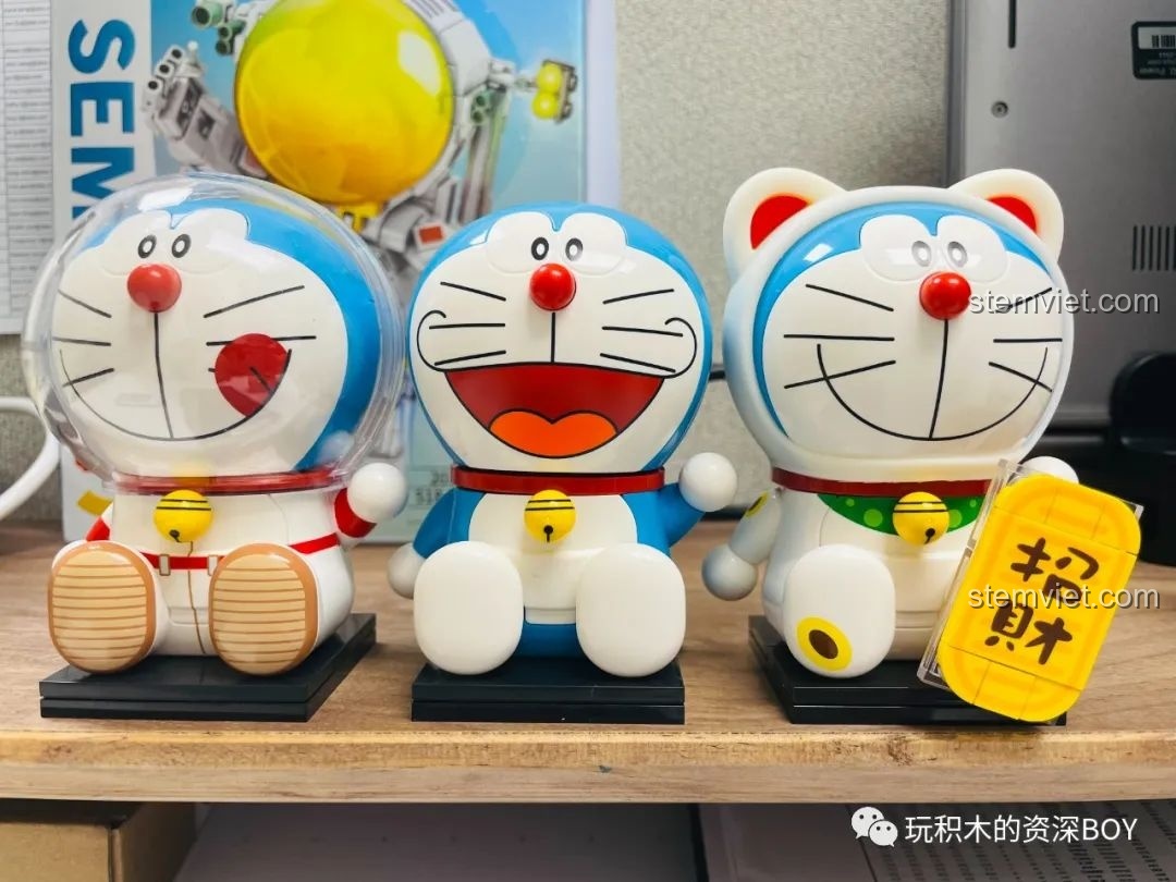 Ba mô hình Doraemon tròn trĩnh Keeppley (phi hành gia, cổ điển, mèo thần tài) đã hoàn thiện, xếp cạnh nhau trên kệ gỗ, tạo thành bộ sưu tập đáng yêu.