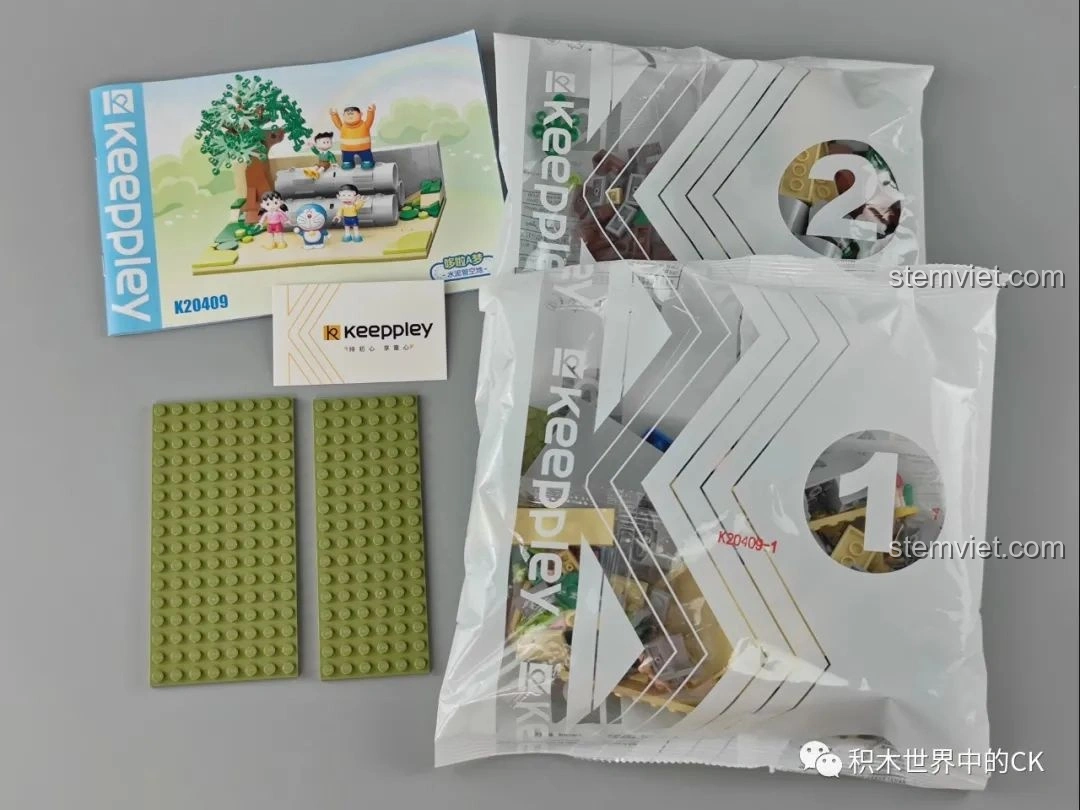 Nội dung bên trong hộp bộ lắp ghép Keeppley K20409 Sân Chơi Ống Cống Doraemon, bao gồm các túi mảnh ghép, sách hướng dẫn và đế lắp.