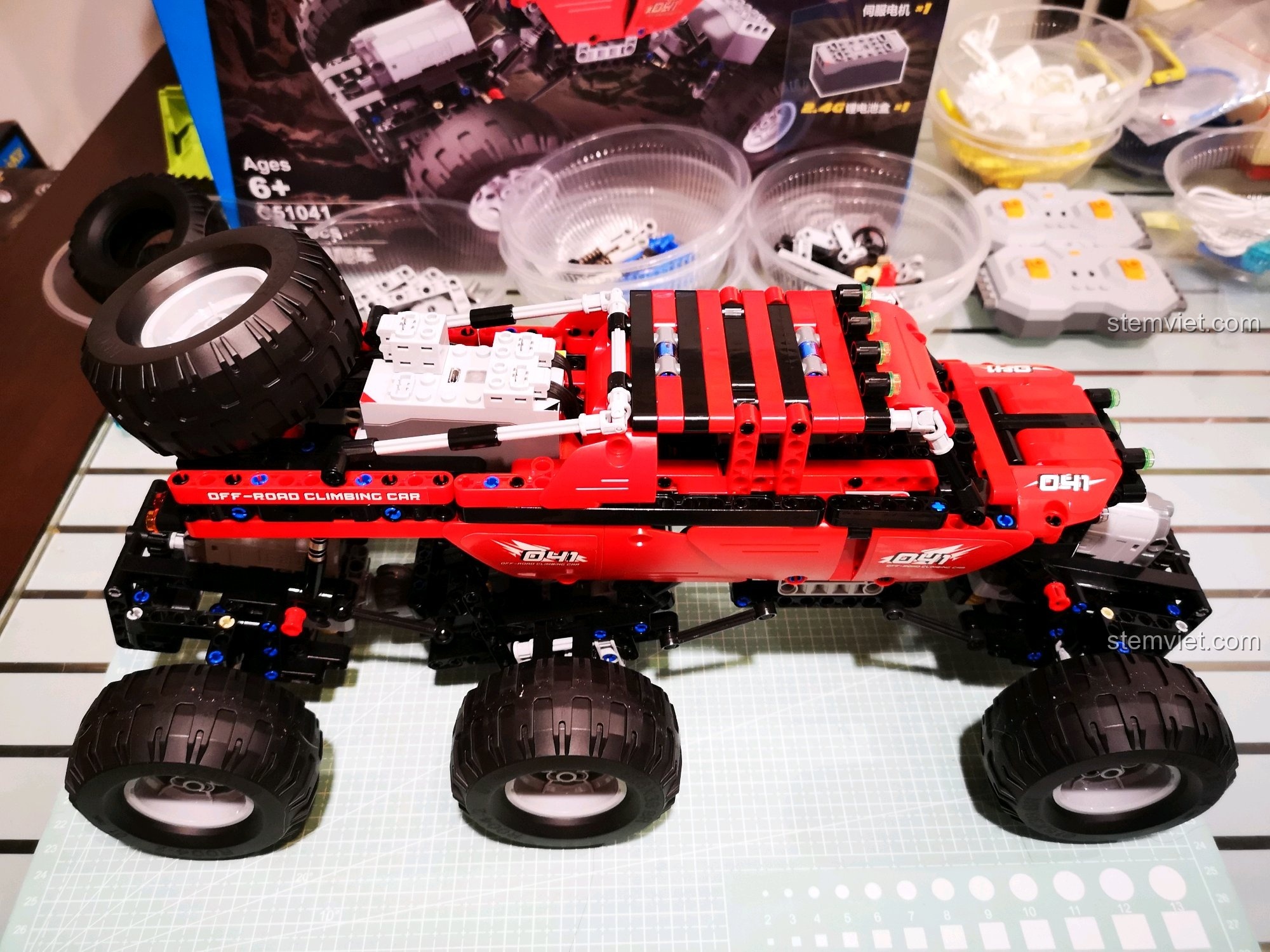 Góc nhìn khác của xe địa hình CaDA C51041 MOC 6x6 màu đỏ, với hộp sản phẩm phía sau, thể hiện sự mạnh mẽ và hầm hố. Cảm nhận CaDA 1041 Xe Leo Núi Địa Hình.