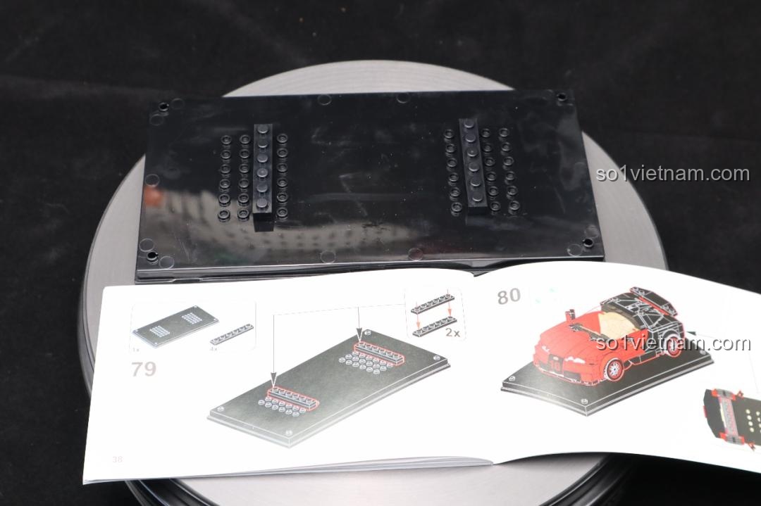 Mô hình Bugatti Veyron Mould King 27027 trong hộp mica, đặt cạnh một mô hình xe khác màu vàng cũng trong hộp mica.