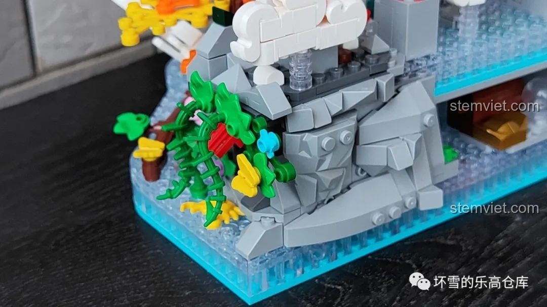 Chi tiết phần núi bên cạnh thác nước của bộ lắp ráp Pantasy 18001 Cá chép hóa rồng, với cây cối và hoa lá xanh tươi.