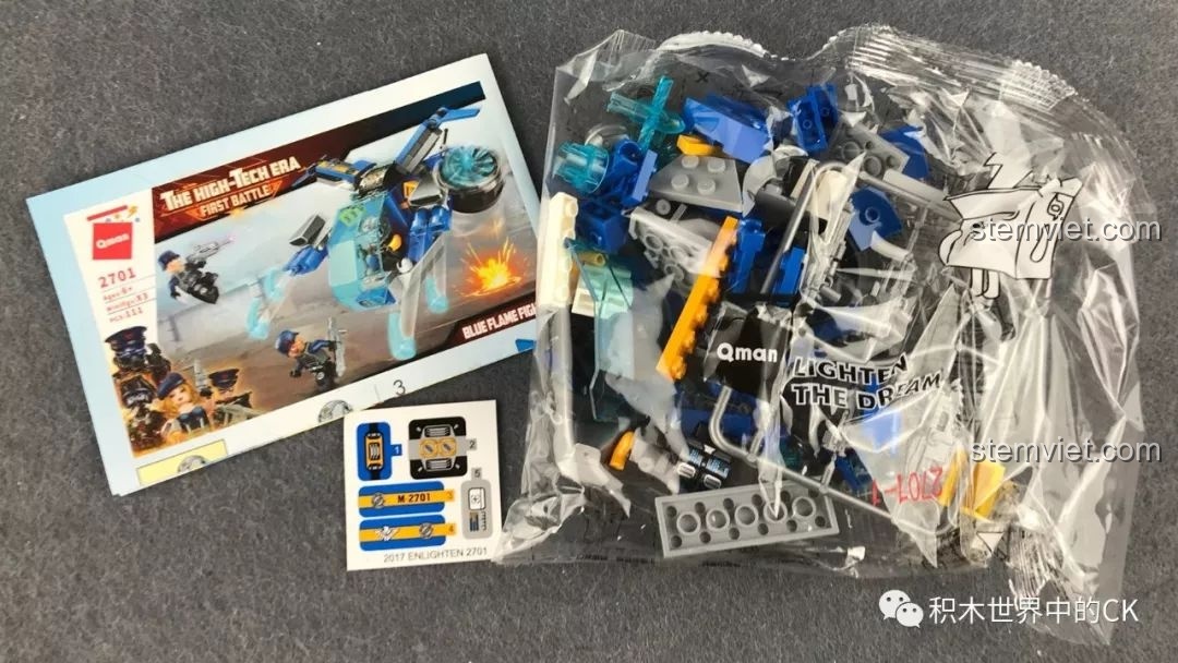 Mở hộp bộ đồ chơi lắp ráp QMAN 2701 Chiến Đấu Cơ Ngọn Lửa Xanh, bao gồm sách hướng dẫn, túi mảnh ghép và sticker.
