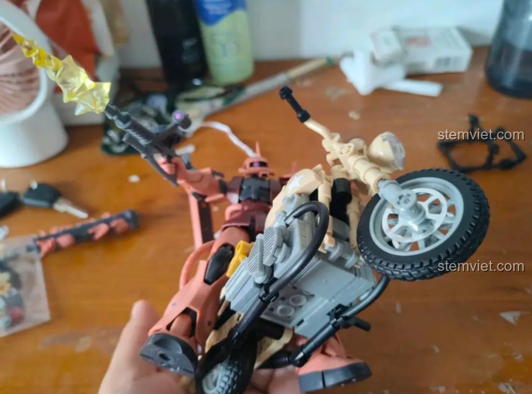 Mô hình Sluban M38-B0959 Mô tô R75 tỉ lệ 1:12 và nhân vật Zaku đang cầm súng, tạo cảnh hành động.