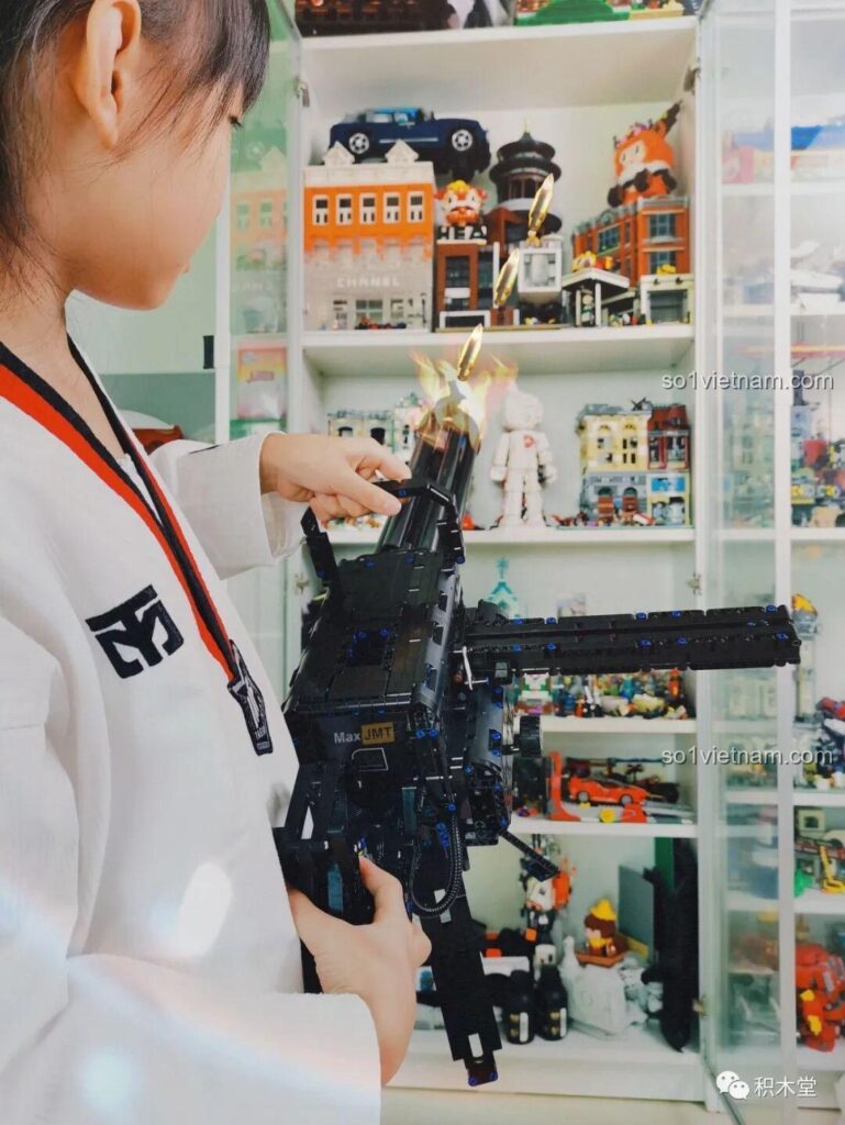 Bé gái đang cầm và chơi với mô hình súng Gatling Taigao Le T2036 đã lắp ráp hoàn chỉnh, thể hiện tính năng động cơ của đồ chơi lắp ráp súng máy Gatling.