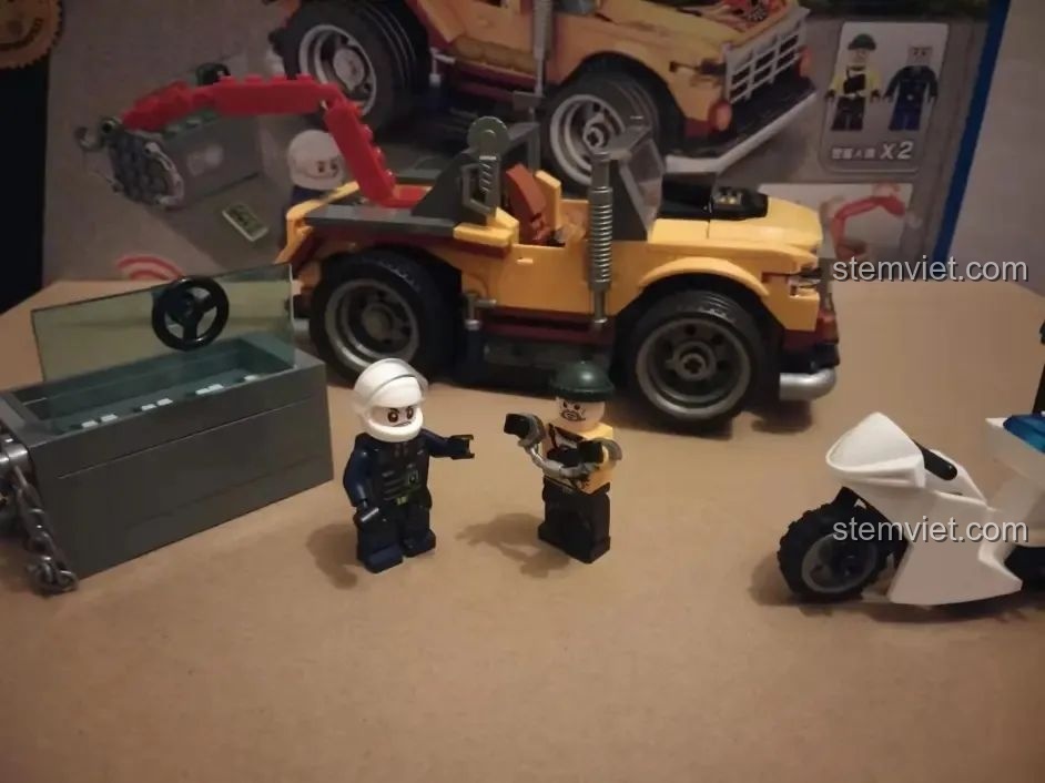 Cảnh sát và tên cướp đối mặt, với két sắt và mô tô cảnh sát trong bộ đồ chơi Xe Cảnh Sát Cứu Hộ Điều Khiển Từ Xa HA389120.