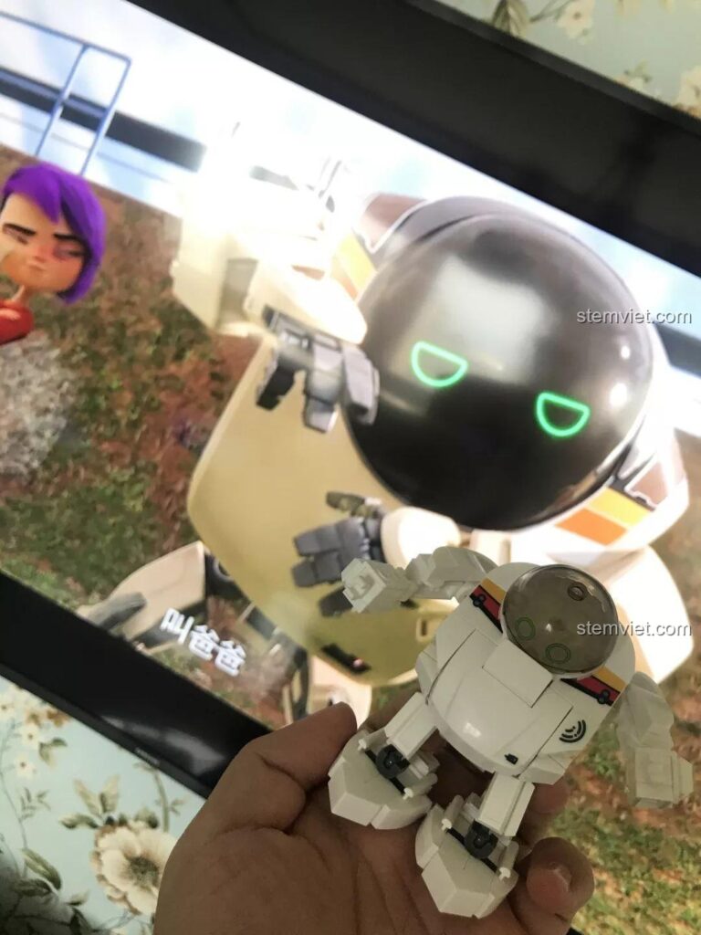 Robot Q-Bricks Sluban M38-B0761E đang được cầm trên tay, so sánh với hình ảnh robot 7723 trong phim Future Robot City. Đánh giá Sluban M38-B0761E Robot Q-dễ thương.