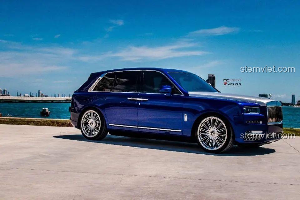 Rolls-Royce Cullinan đời thực màu xanh dương với vành xe mạ chrome, đỗ bên bờ biển dưới trời xanh.