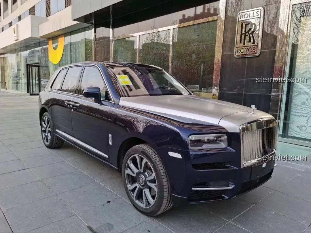 Rolls-Royce Cullinan đời thực màu xanh đen với nắp capo bạc, đỗ trước tòa nhà sang trọng.