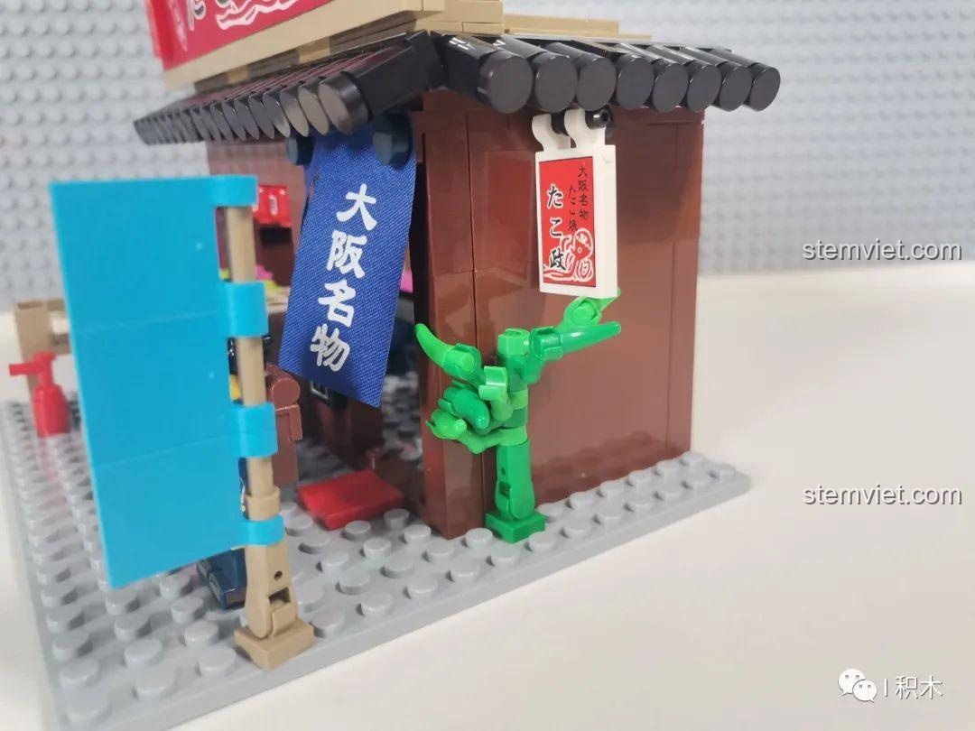 Góc nhìn bên hông của mô hình Cửa hàng Takoyaki Osaka SEMBO 601072, cho thấy chi tiết cây xanh và cấu trúc.