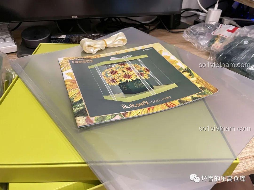 Các phụ kiện đi kèm bộ lắp ráp Hộp Quà Bó Hoa Hướng Dương Về Phía Mặt Trời 601223 gồm ruy băng, thiệp, và hộp trong suốt.