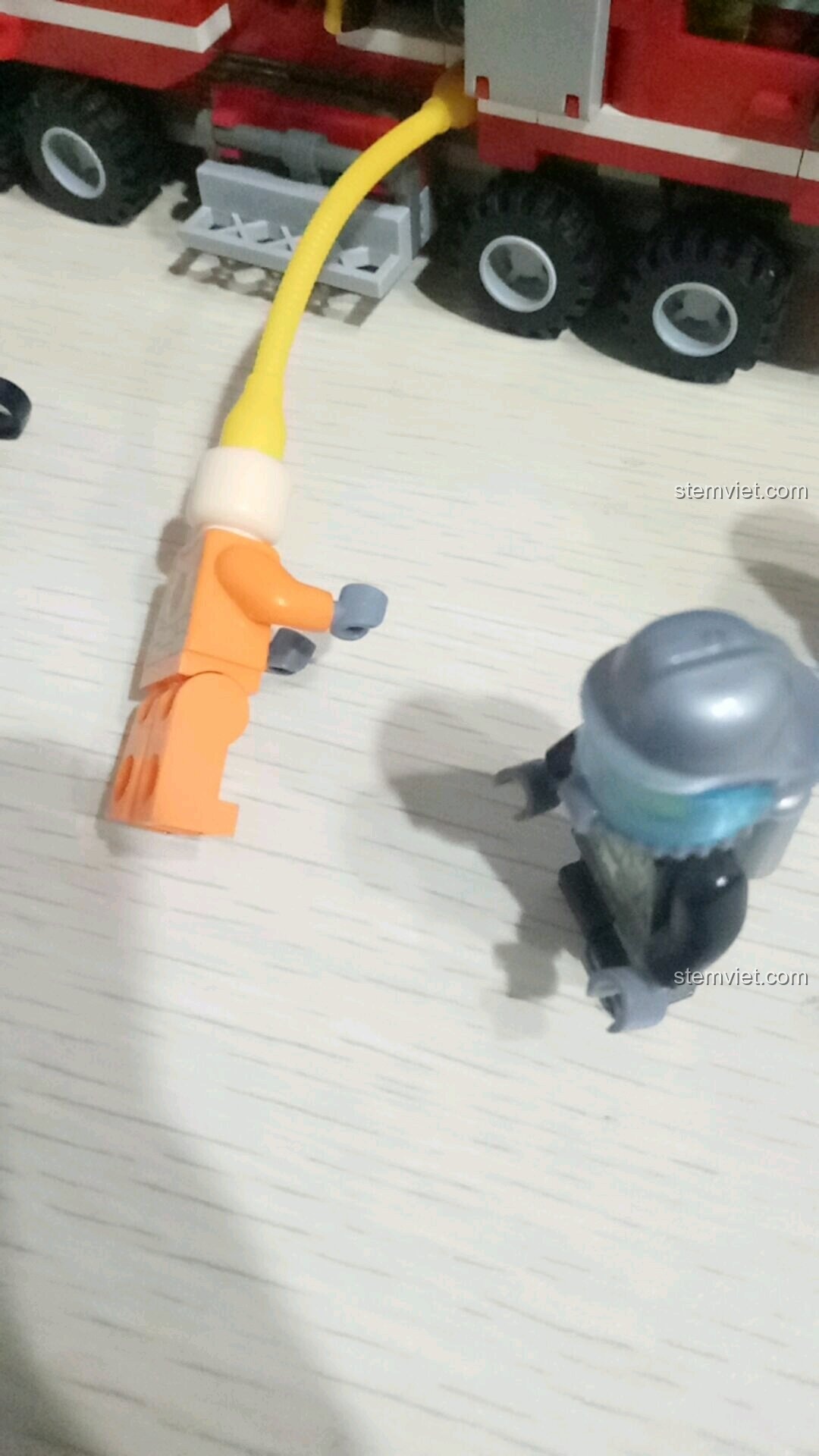 Minifigure lính cứu hỏa đang hướng vòi rồng vào đồng đội trong kịch bản cứu hỏa của bộ SEMBO 603034.