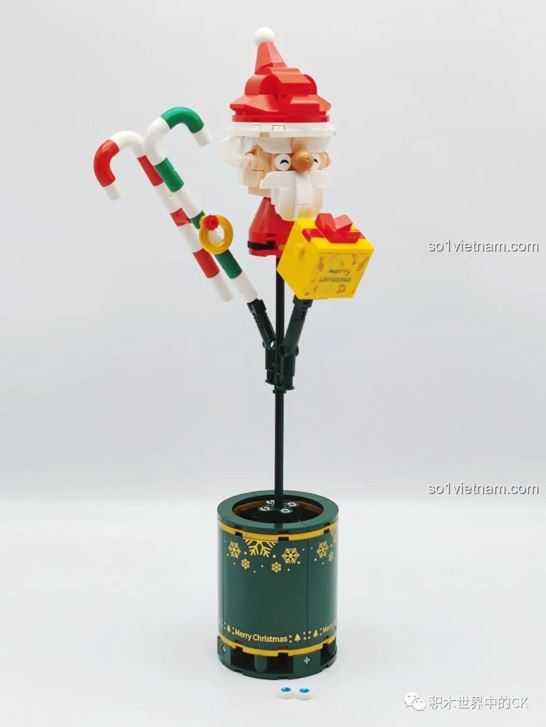 Quá trình lắp ráp bộ SEMBO 605026 Bó Hoa Giáng Sinh, với ông già Noel và kẹo gậy được gắn vào đế màu xanh lá.