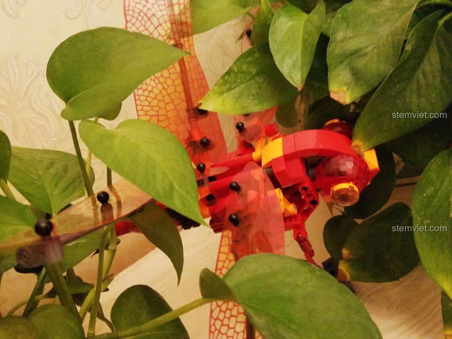 Mô hình Chuồn Chuồn Đỏ Cơ Khí Sembo 703300 ẩn mình trong cây xanh, tạo cảnh quan tự nhiên.