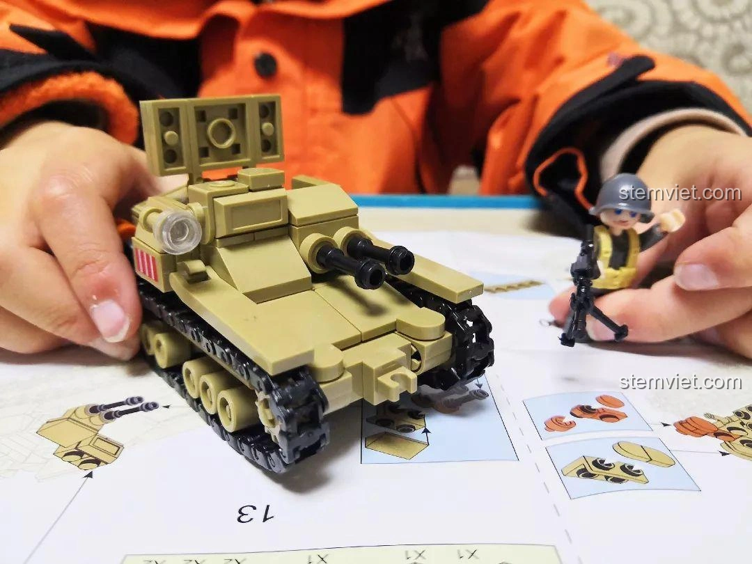 Bé trai đang cầm mô hình Sluban M38-B0709 Xe Tăng Siêu Nhẹ CV33 đã hoàn thành, thể hiện niềm vui và thành quả.