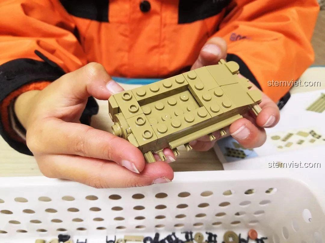 Bé trai đang cầm phần thân xe tăng đã lắp ráp của bộ đồ chơi Sluban M38-B0709 Xe Tăng Siêu Nhẹ CV33, thể hiện sự tiến bộ trong quá trình lắp.