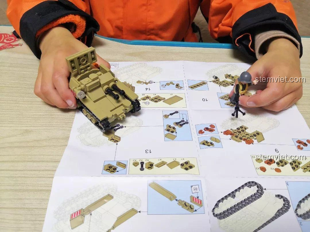 Bé trai đang lắp ráp những chi tiết cuối cùng của mô hình Sluban M38-B0709 Xe Tăng Siêu Nhẹ CV33, với minifigure đứng cạnh.