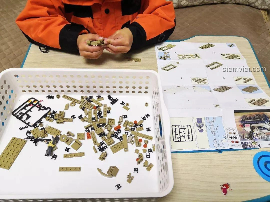 Một bé trai đang tập trung lắp ráp phần thân của mô hình Sluban M38-B0709 Xe Tăng Siêu Nhẹ CV33, với các mảnh ghép và sách hướng dẫn.