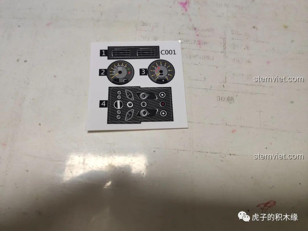 Cận cảnh tấm sticker đi kèm bộ lắp ráp C001, bao gồm đồng hồ tốc độ và các nút bấm trên bảng điều khiển.