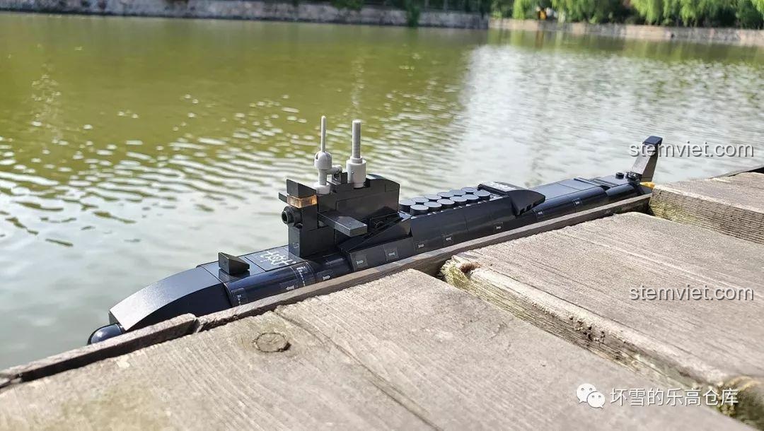 Mô hình tàu ngầm Sluban M38-B0703 đặt trên cầu gỗ, một phần chìm dưới mặt nước, tạo hiệu ứng chân thực.
