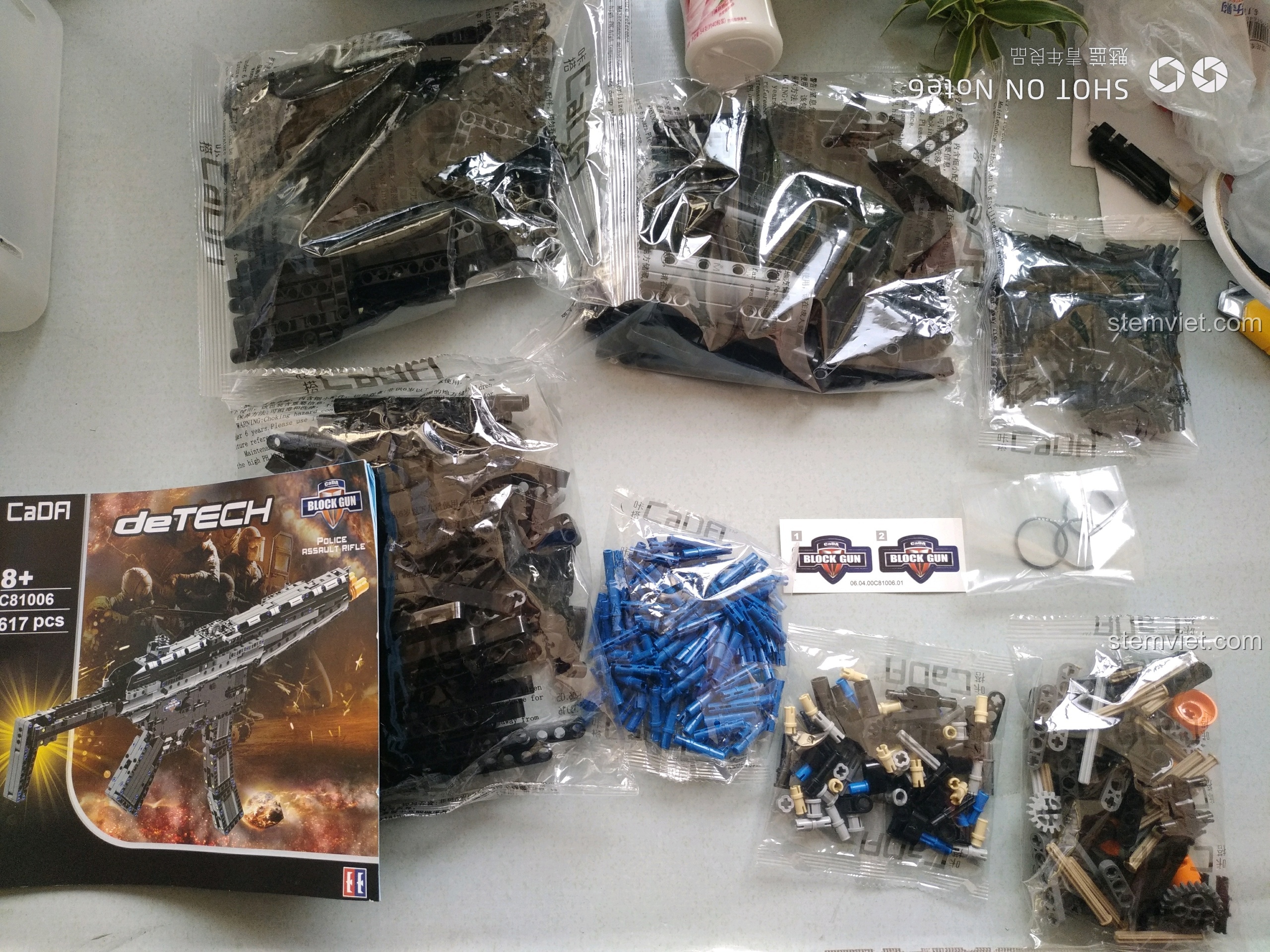 Toàn bộ chi tiết của bộ đồ chơi lắp ráp CaDA 81006 giá bình dân, bao gồm các túi mảnh ghép, sách hướng dẫn và sticker.