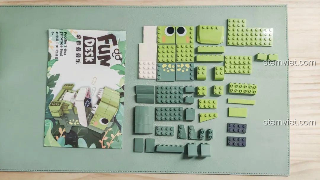 Tổng quan các mảnh ghép và sách hướng dẫn của bộ lắp ghép Khủng long Bạo Chúa Ăn Vặt JAKI JK5102 được bày ra trên bàn.