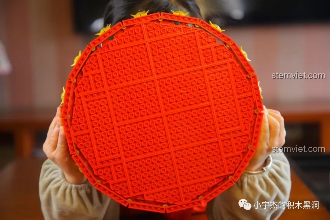 Một bé gái đang khoe thành quả lắp ráp phần đáy của bộ Hộp đựng mứt Tết WOMA C.9122, thể hiện niềm vui thích.