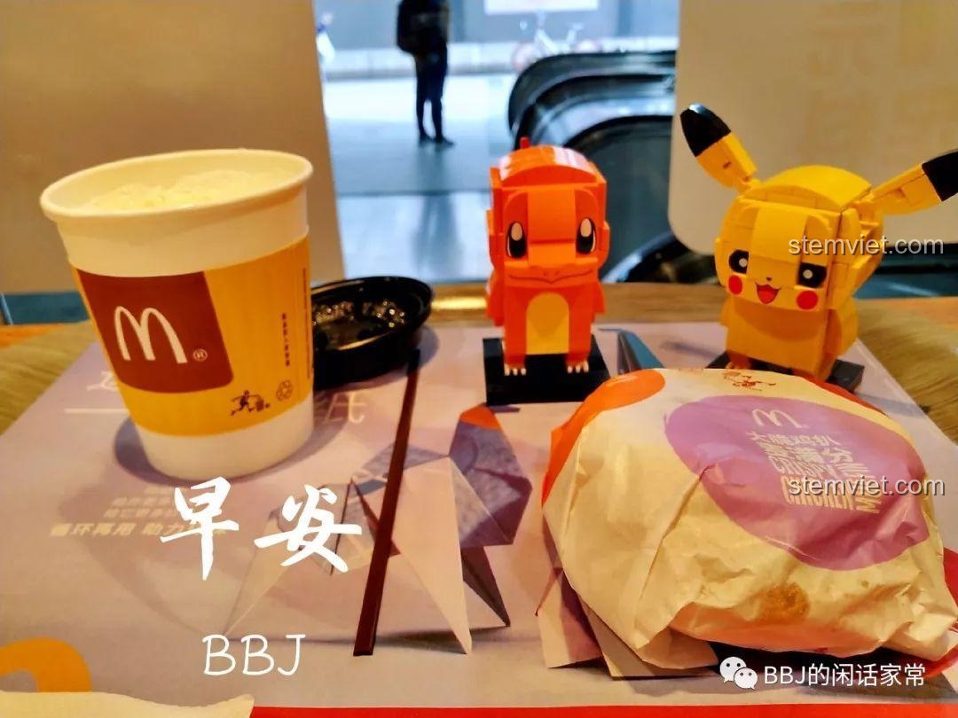 Hai mô hình Pikachu và Charmander được đặt trên bàn ăn cùng với bữa sáng, tạo nên một khung cảnh vui nhộn.