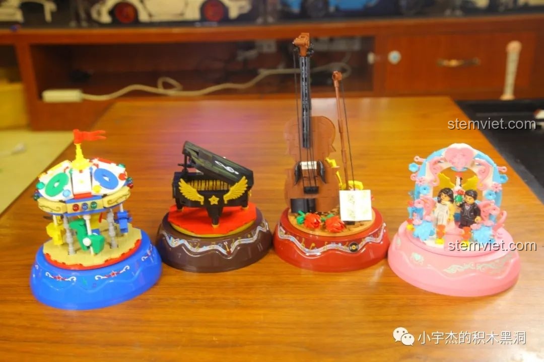 Một góc nhìn khác của bốn mô hình hộp nhạc WOMA đã hoàn thành, sắp xếp theo bố cục khác trên bàn gỗ.