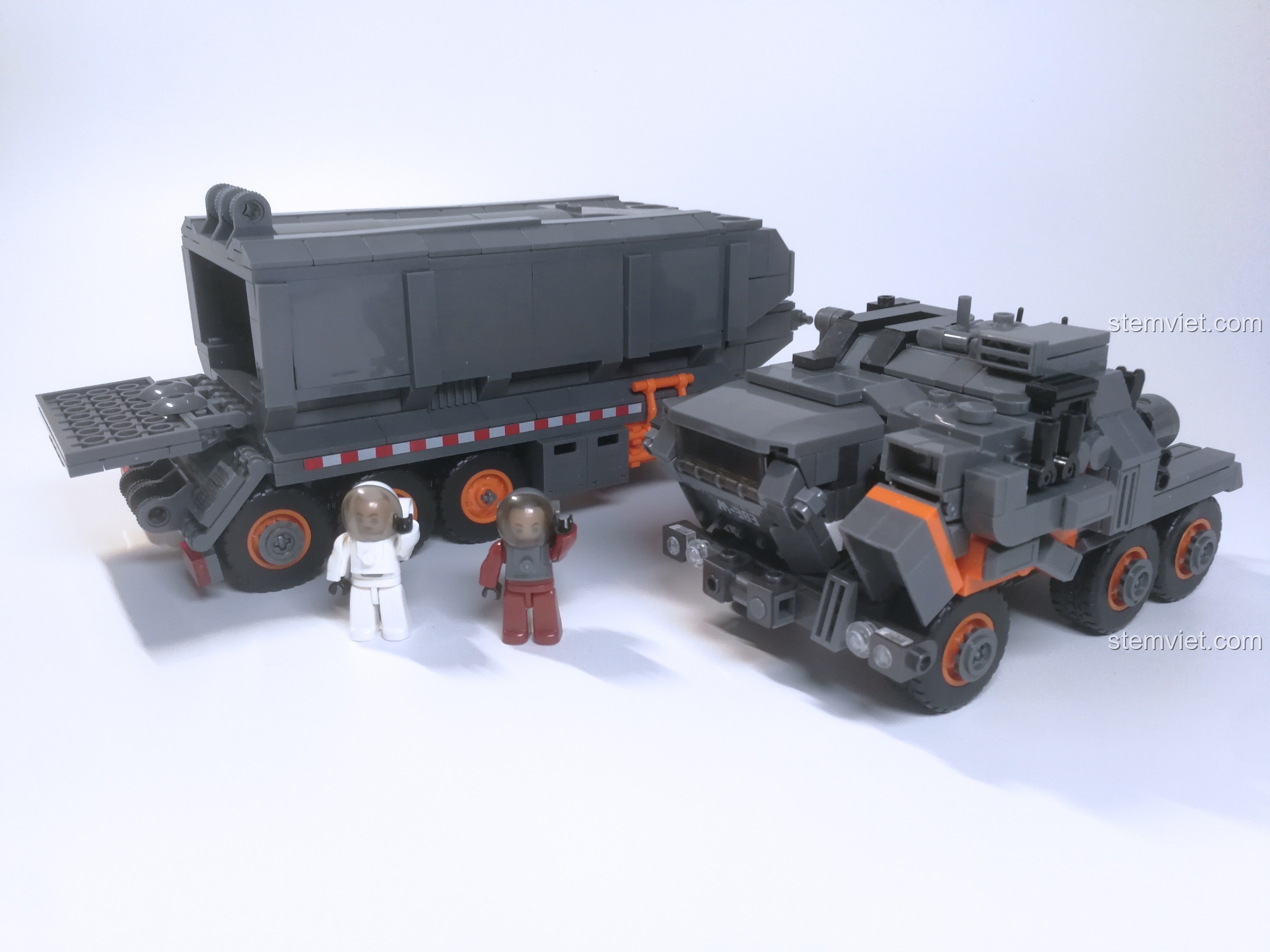 Hai nhân vật phi hành gia đang vẫy tay chào bên cạnh chiếc xe tải Sluban, cửa sau thùng hàng đang mở.