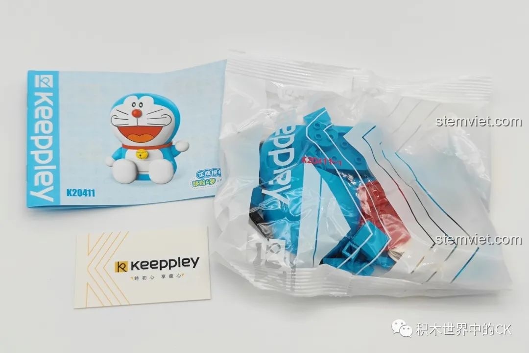 Bên trong hộp Keeppley Doraemon K20411 với túi mảnh ghép, sách hướng dẫn lắp ráp và thẻ thương hiệu Keeppley.