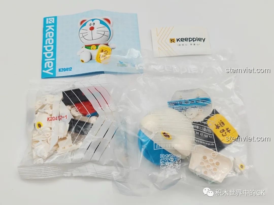 Bên trong hộp Keeppley Doraemon K20412 với túi mảnh ghép, sách hướng dẫn lắp ráp và thẻ thương hiệu Keeppley.