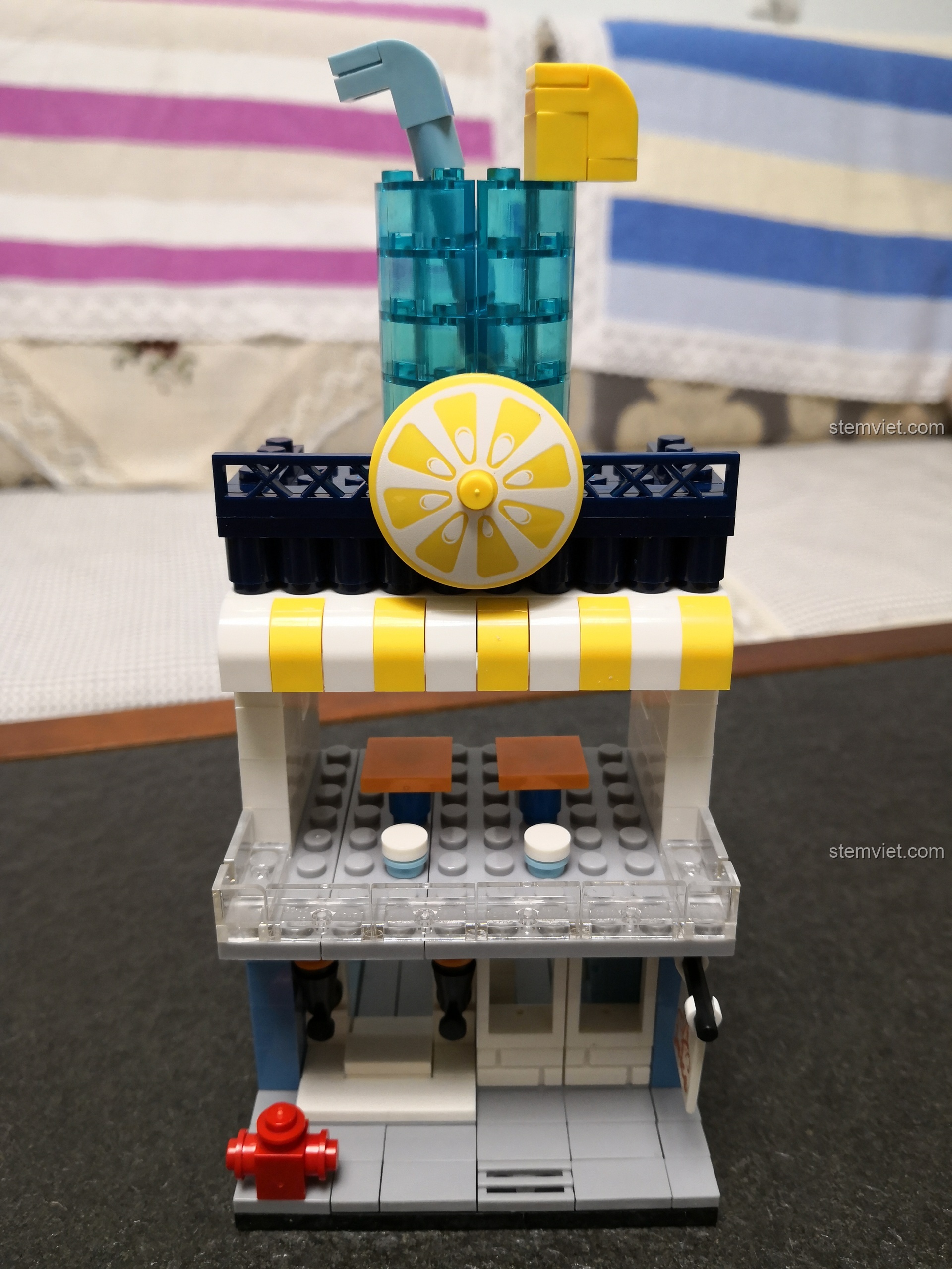 Toàn cảnh mô hình cửa hàng nước ép trái cây mini WANGE 2312, với ly nước lớn và lát chanh trên nóc.