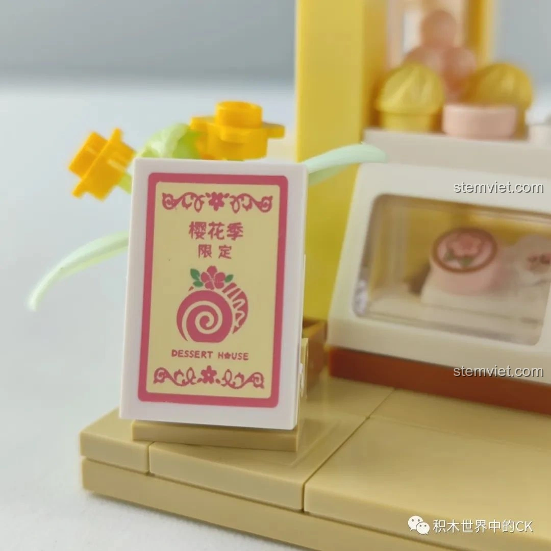 Cận cảnh mô hình mèo con đáng yêu trong bộ lắp ghép Wekki 516601 Tiệm Bánh Ngọt Hoa Anh Đào, đứng trước cửa tiệm.