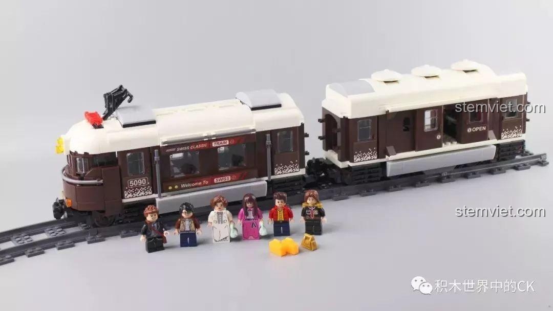 Minifigure đang chờ tàu Winner 5090 Tàu Hỏa Thành Phố Cổ Điển Thụy Sĩ tại sân ga, tạo cảnh quan sống động.