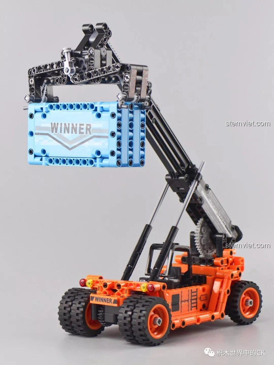 Mô hình hoàn chỉnh Winner 7059 Xe Nâng Gắp Container màu cam đen đang gắp container xanh dương, sẵn sàng trưng bày.