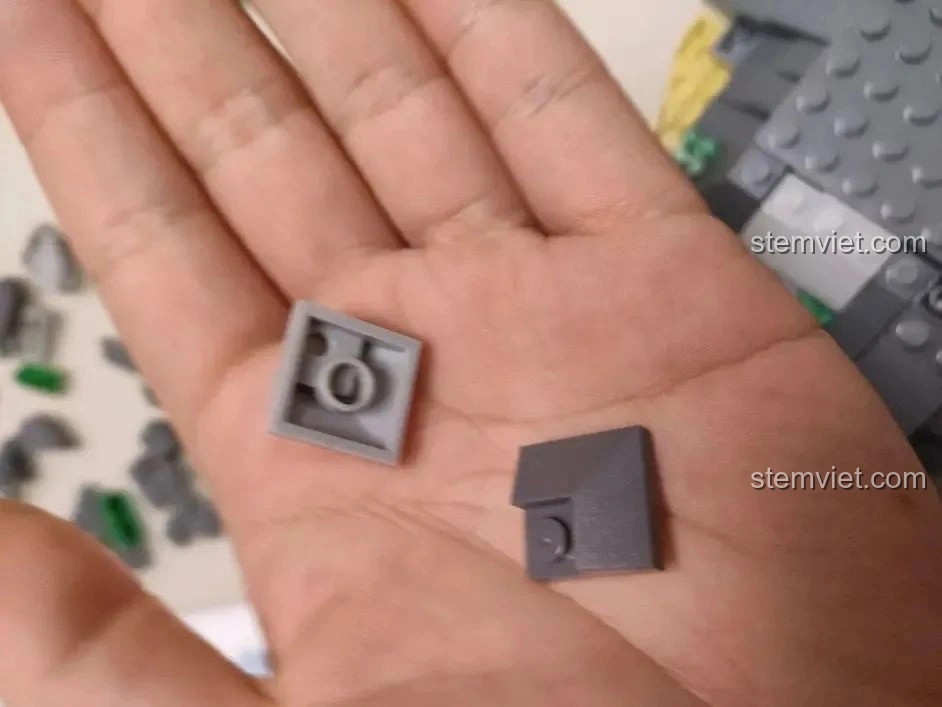 Hai mảnh ghép màu xám khác nhau của bộ WOMA C0348 Đình Phượng Sơ trên lòng bàn tay, thể hiện sự đa dạng chi tiết.