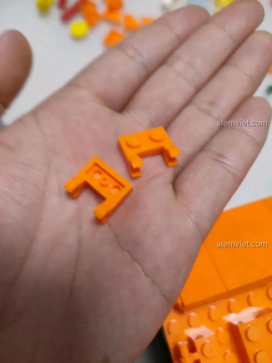 Hai mảnh ghép màu cam hình chữ L của bộ WOMA C0348 Đình Phượng Sơ trên lòng bàn tay, dùng cho cấu trúc.