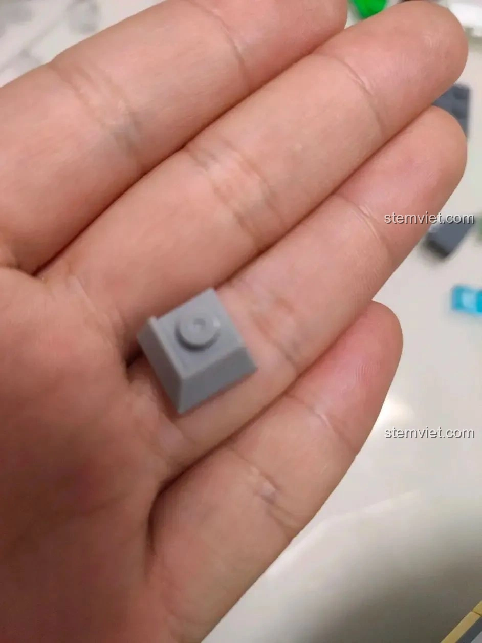 Một mảnh ghép góc màu xám của bộ WOMA C0348 Đình Phượng Sơ trên lòng bàn tay, cho thấy độ sắc nét.