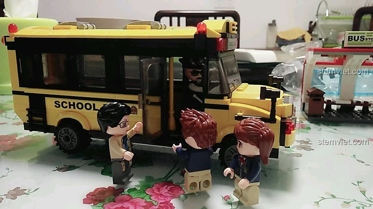 Chiếc xe buýt trường học màu vàng đã hoàn thành, bác tài xế ngồi trong xe, cô giáo và học sinh đang xếp hàng lên xe trong bộ QMAN 1136.