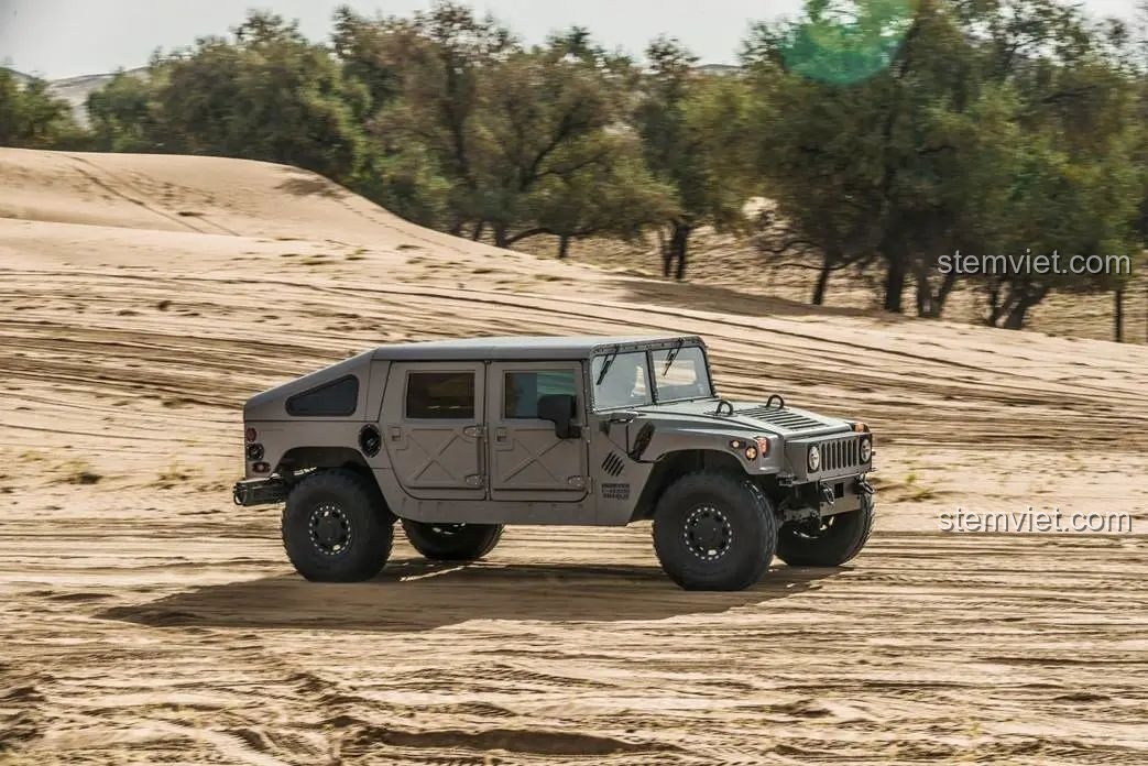 Chiếc xe Humvee H1 màu xám cát đang chạy trên sa mạc, thể hiện khả năng vượt địa hình ấn tượng của xe.