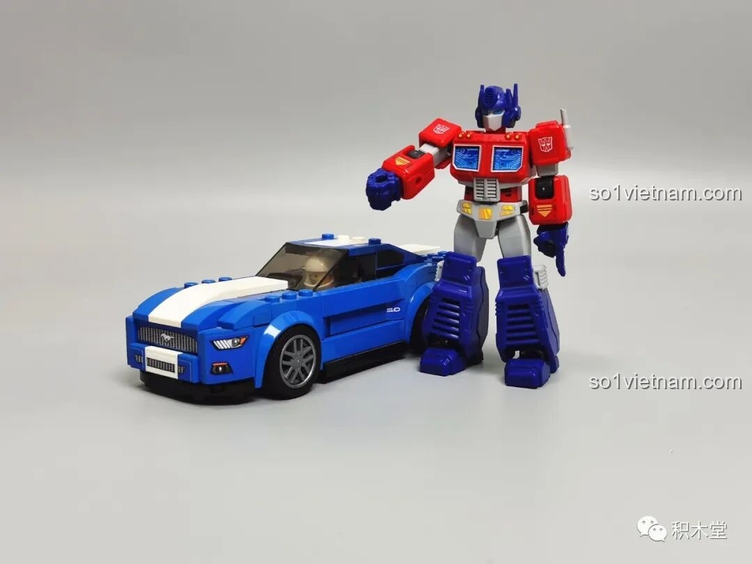 Figure Optimus Prime BLOKEES 71100 đứng cạnh mô hình xe Ford Mustang, so sánh kích thước với dòng Speed Champions.