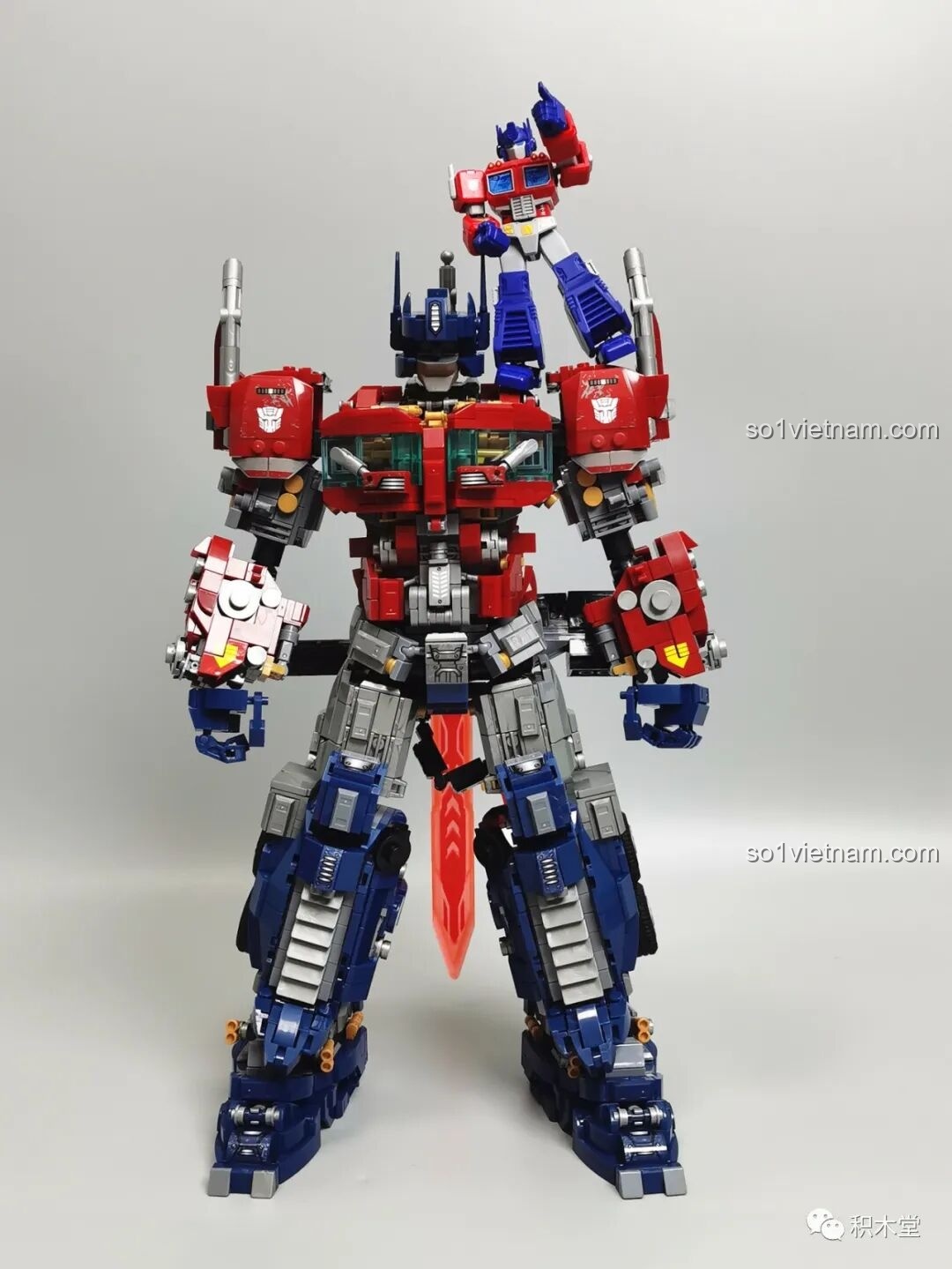 Figure Optimus Prime nhỏ của BLOKEES 71100 ngồi trên vai của phiên bản lớn, tạo ra một hình ảnh vui nhộn.
