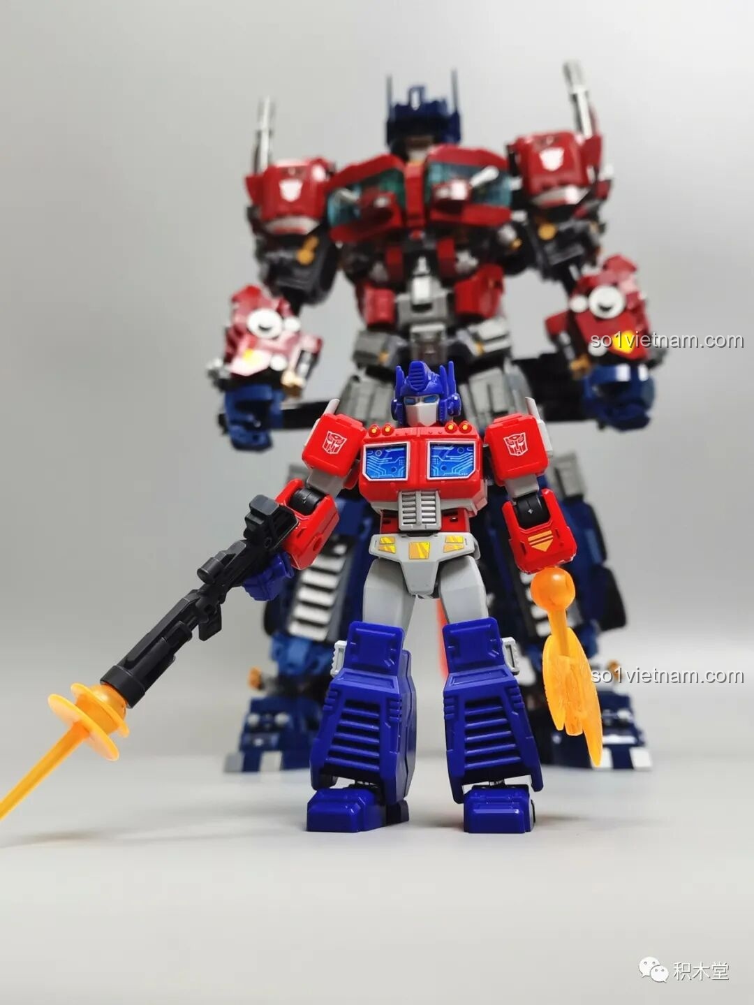 Figure Optimus Prime BLOKEES 71100 đứng cạnh một phiên bản Optimus Prime lớn hơn nhiều, cho thấy sự khác biệt về kích thước.