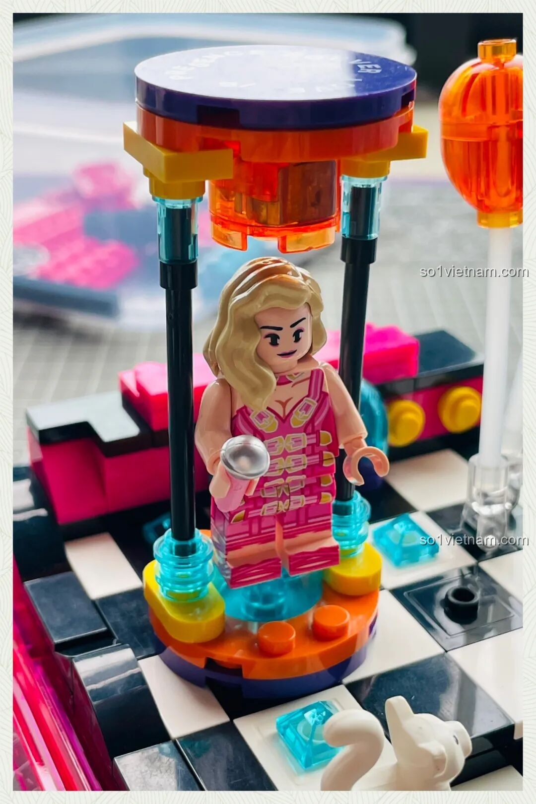 Minifigure ca sĩ tóc vàng đang đứng trên bục biểu diễn của sân khấu Ái Vũ Đài AREA-X AB0006, trong quá trình lắp ráp.