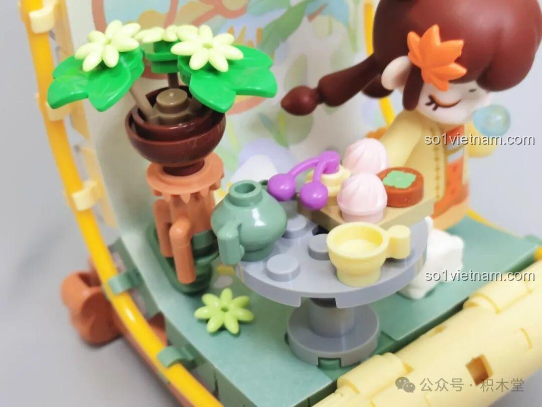 Ảnh chụp cận cảnh bàn trà trong mô hình Nanci mùa Thu, với ấm trà, chén, bánh ngọt và cây bonsai được tạo hình chi tiết.